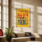 A framed art print with the Spanish text 'SOLO EL PUEBLO SALVA AL PUEBLO' in red, orange, and blue lettering on a yellow background, displayed on a beige wall in a modern living room setting.