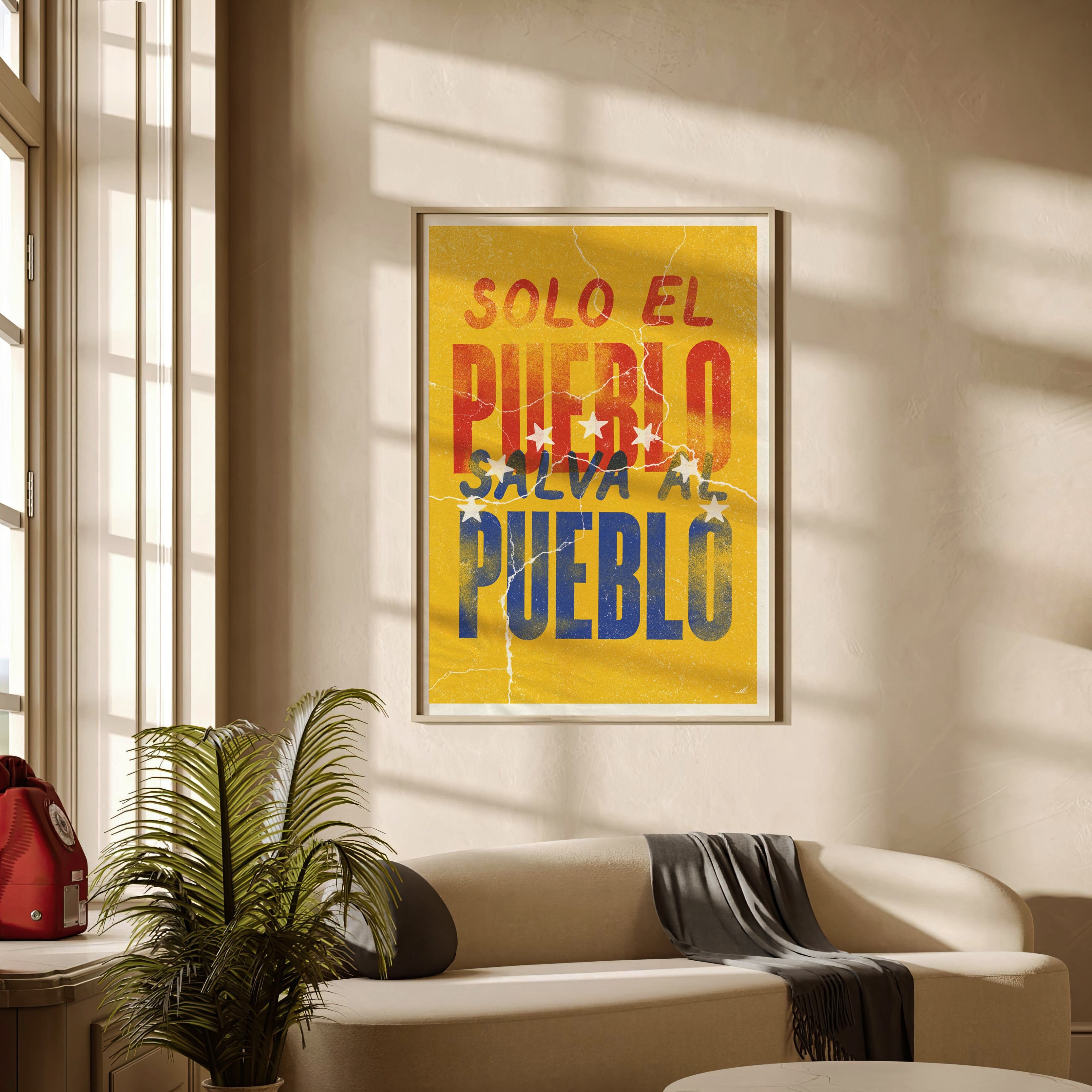A framed art print with the Spanish text 'SOLO EL PUEBLO SALVA AL PUEBLO' in red, orange, and blue lettering on a yellow background, displayed on a beige wall in a modern living room setting.
